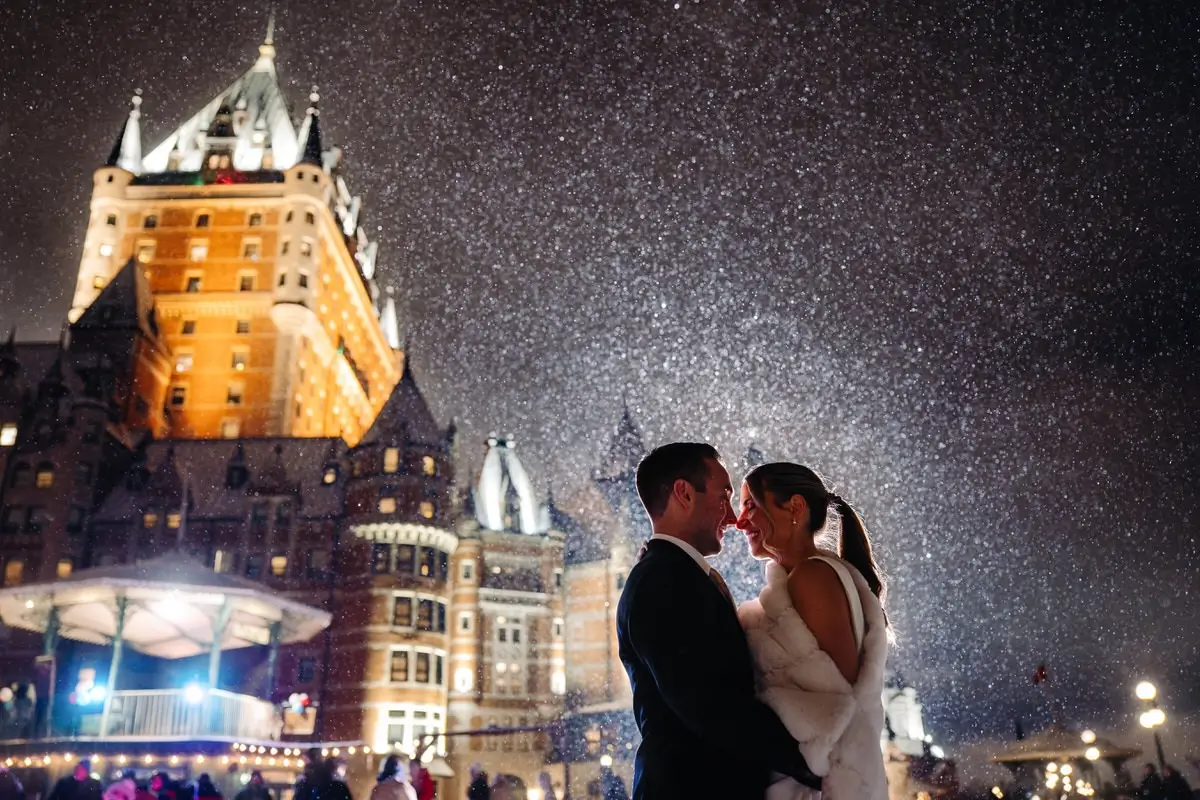 Bride and groom under the snowflakes at night in front of the Chateau Frontenac
