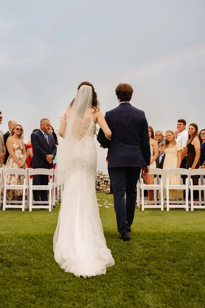Bride going down the aisle with a rainbow over them at the Manoir Richelieu's golf course