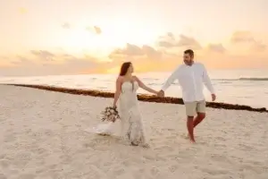 Un couple de mariés qui marche sur la plage du Sandos Playacar au lever du soleil