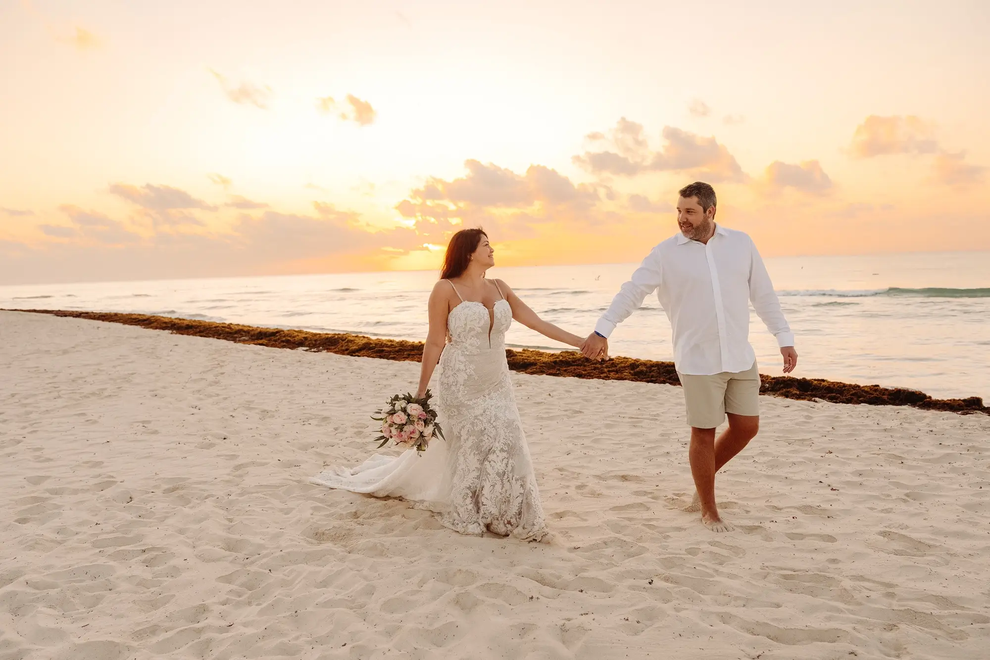 Un couple de mariés qui marche sur la plage du Sandos Playacar au lever du soleil