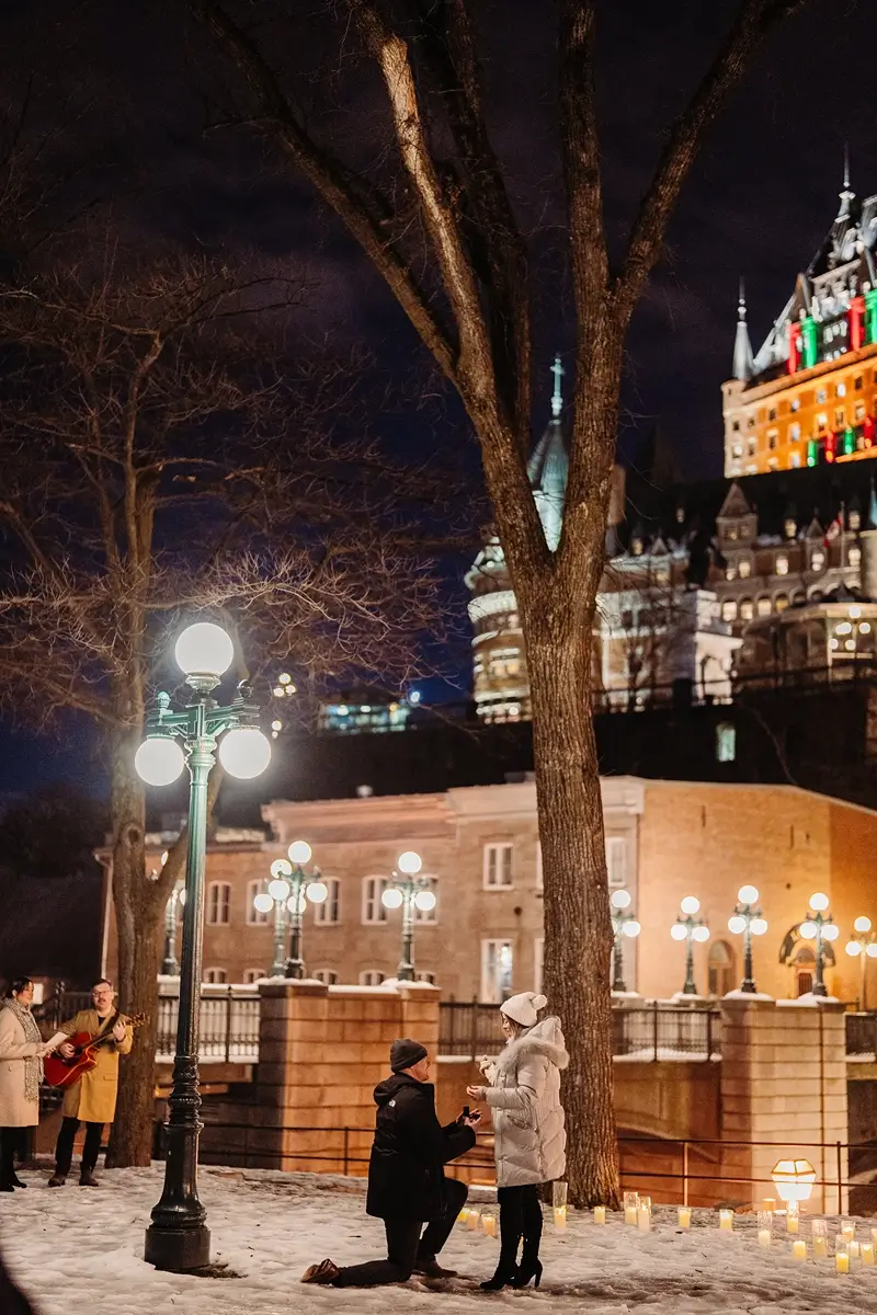 Guy on one knee for a surprisal proposal with musicians in front of the Chateau Frontenac